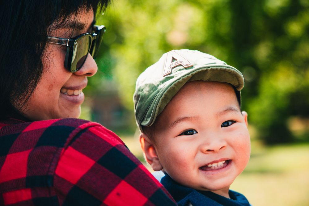 Smiling person in a red and black plaid shirt and baseball cap enjoying a sunny day outdoors.