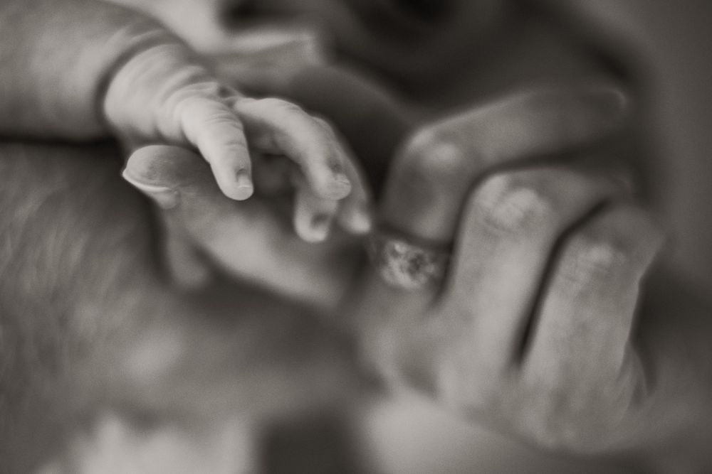 A tender black and white close-up photograph of two hands gently touching and connecting.
