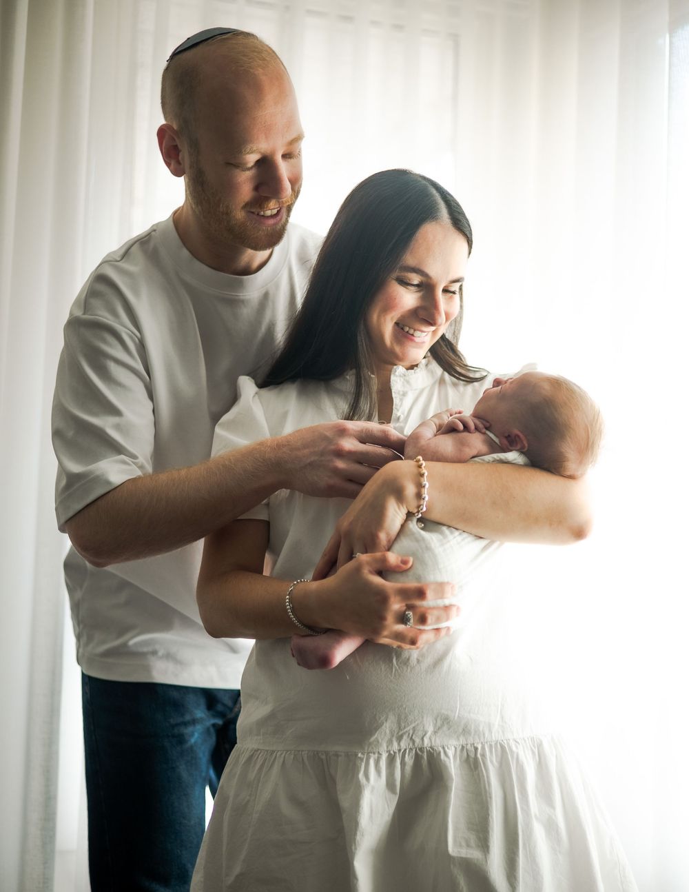 Three candid moments show a tender interaction between parent and baby in white clothing by a bright window.