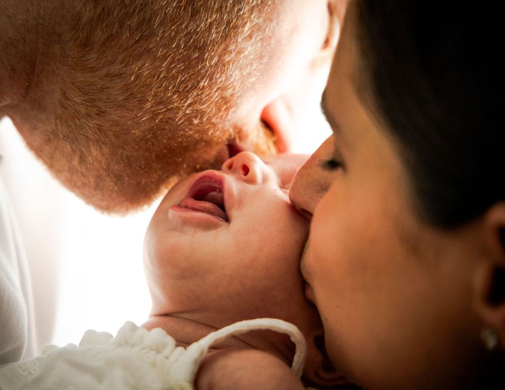 A couple shares an intimate kiss in front of a bright window with soft lighting.