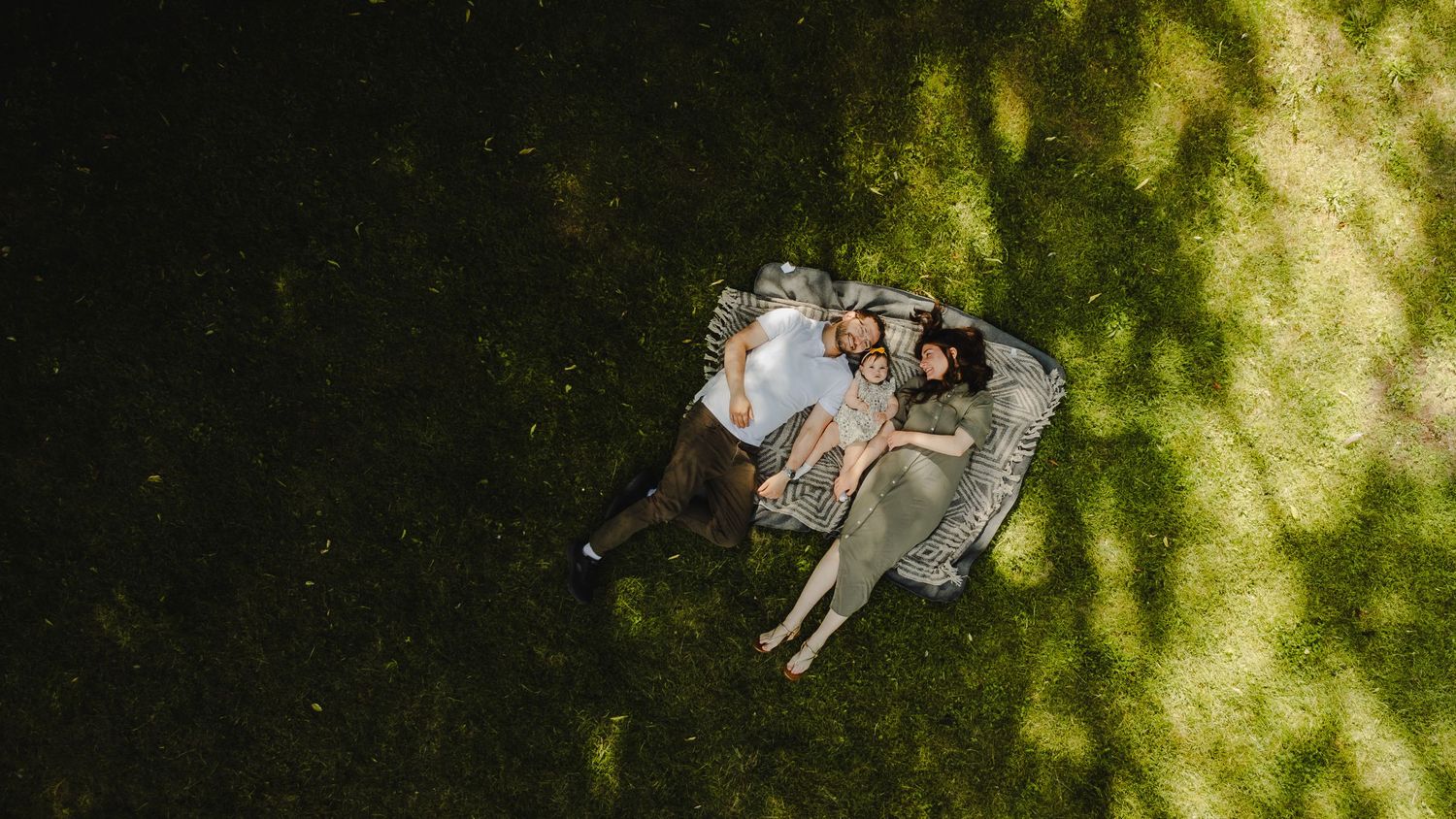 Aerial view of a couple relaxing on a blanket in lush green grass, enjoying a peaceful outdoor picnic.