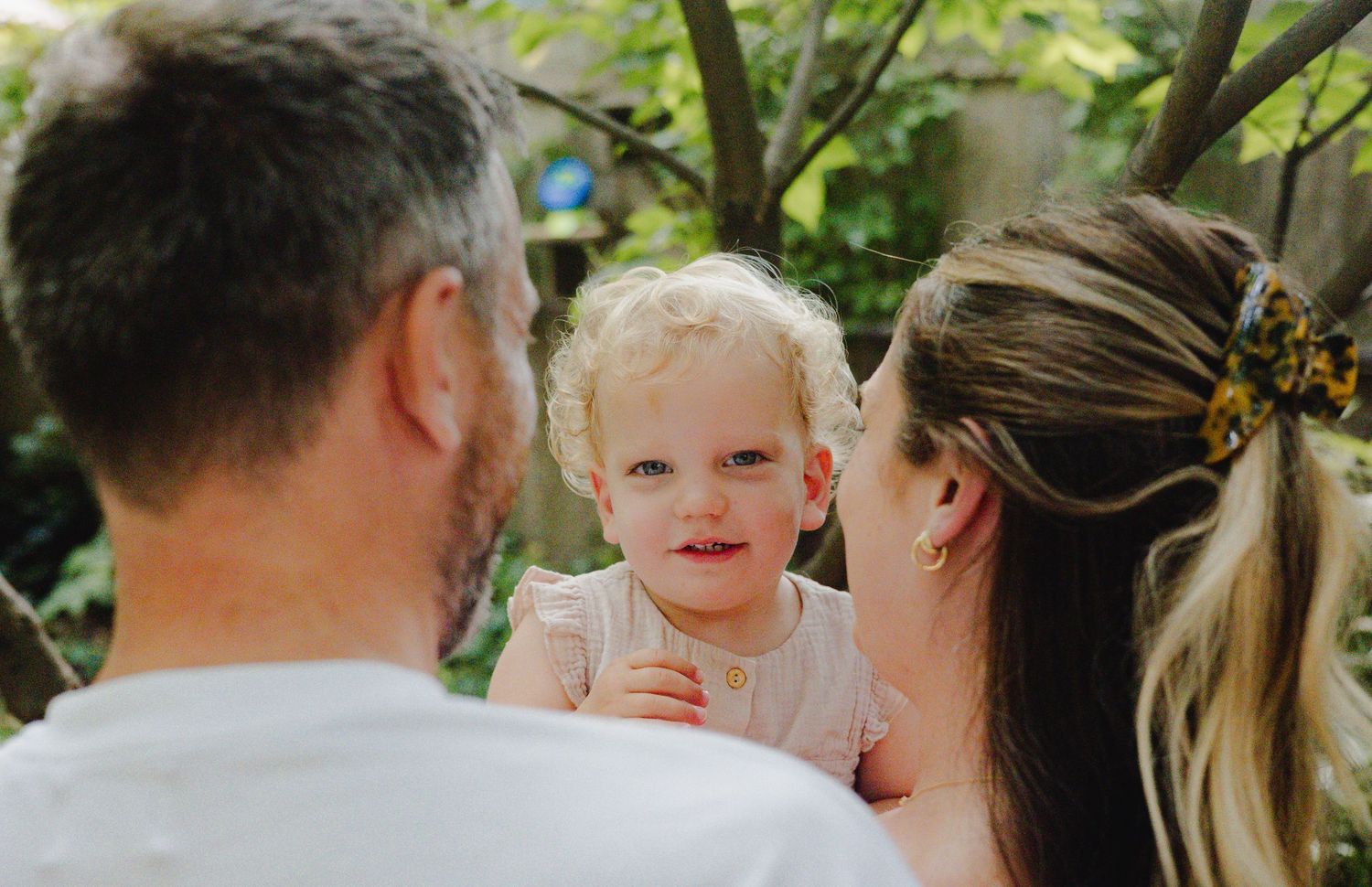 A candid outdoor family moment with a child amidst greenery and sunlight.