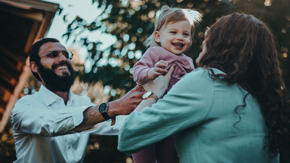 Family enjoying a playful moment outdoors in a garden setting with warm lighting.
