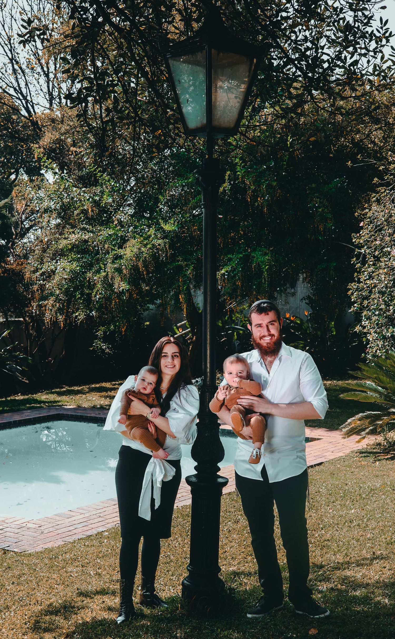 Family portrait session in garden setting with vintage lamp post and trees.