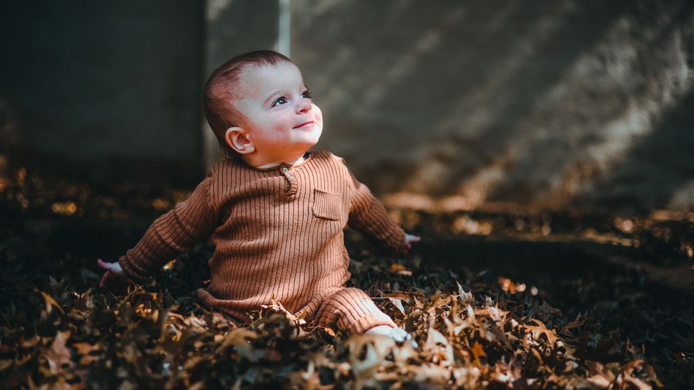 Baby sitting in autumn leaves during outdoor photo session.