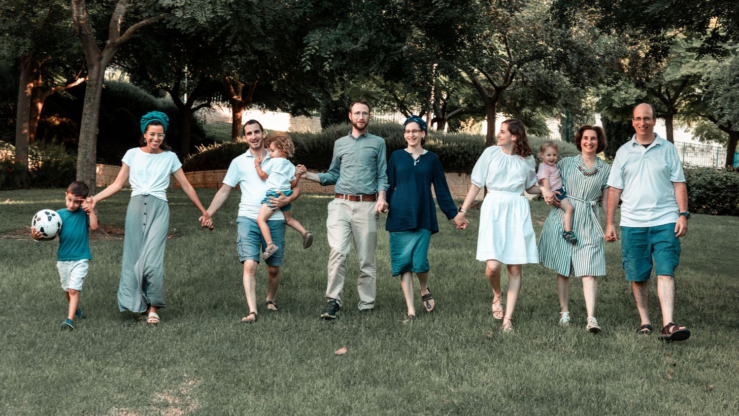 Group of people in coordinated blue and white outfits holding hands while walking on grass.