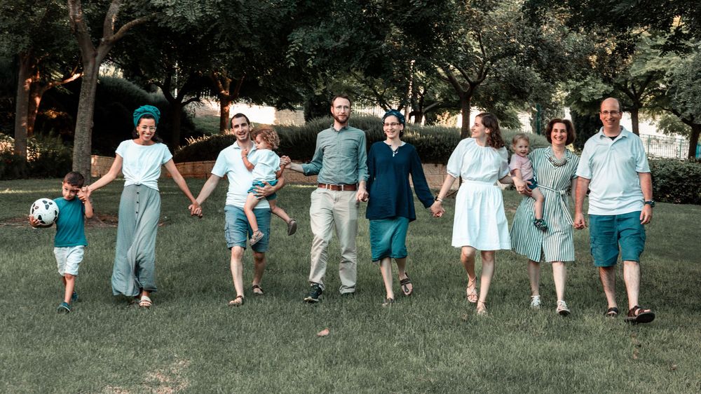 Group of people in coordinated blue and white outfits holding hands while walking on grass.