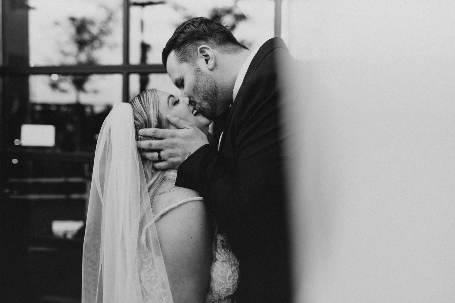 A black and white romantic wedding moment captured in an intimate close-up shot with the couple sharing a tender kiss.