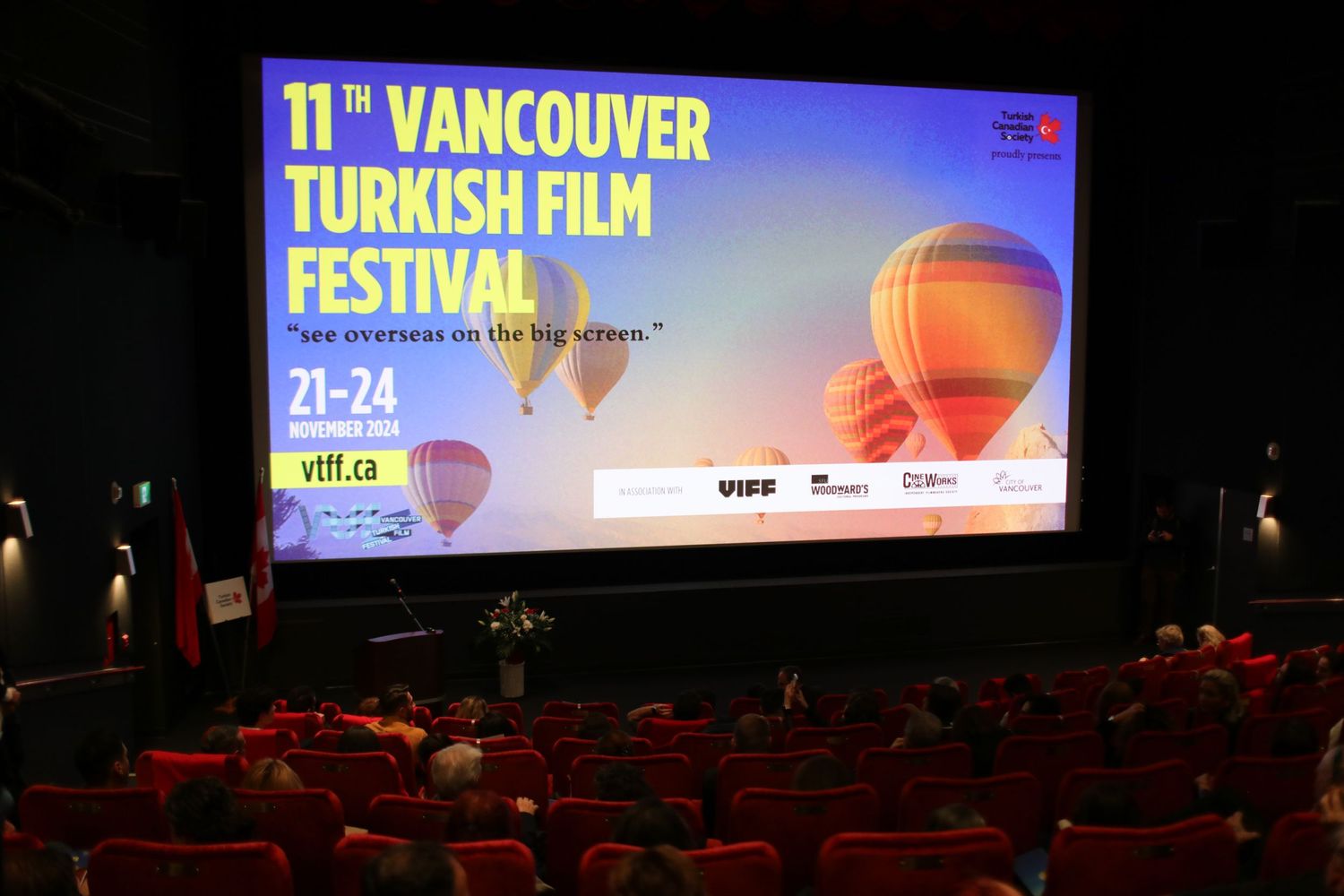 Movie theater screen displays Vancouver Turkish Film Festival banner with colorful hot air balloon graphics in dimly lit cinema.
