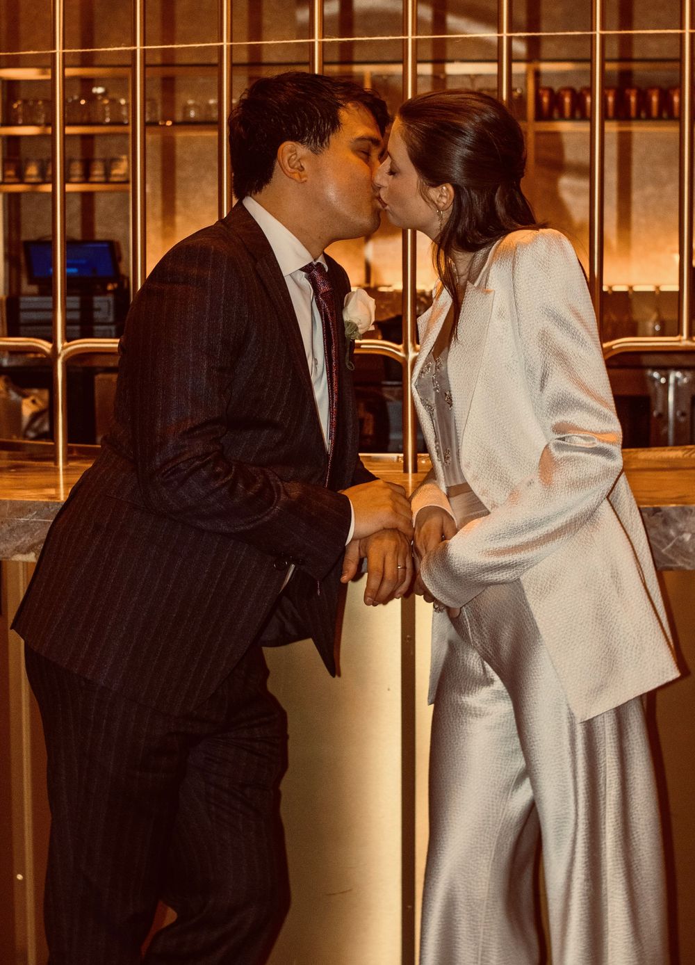 Couple sharing a romantic kiss at a bar during their Las Vegas wedding, groom in pinstripe suit, bride in white blazer.