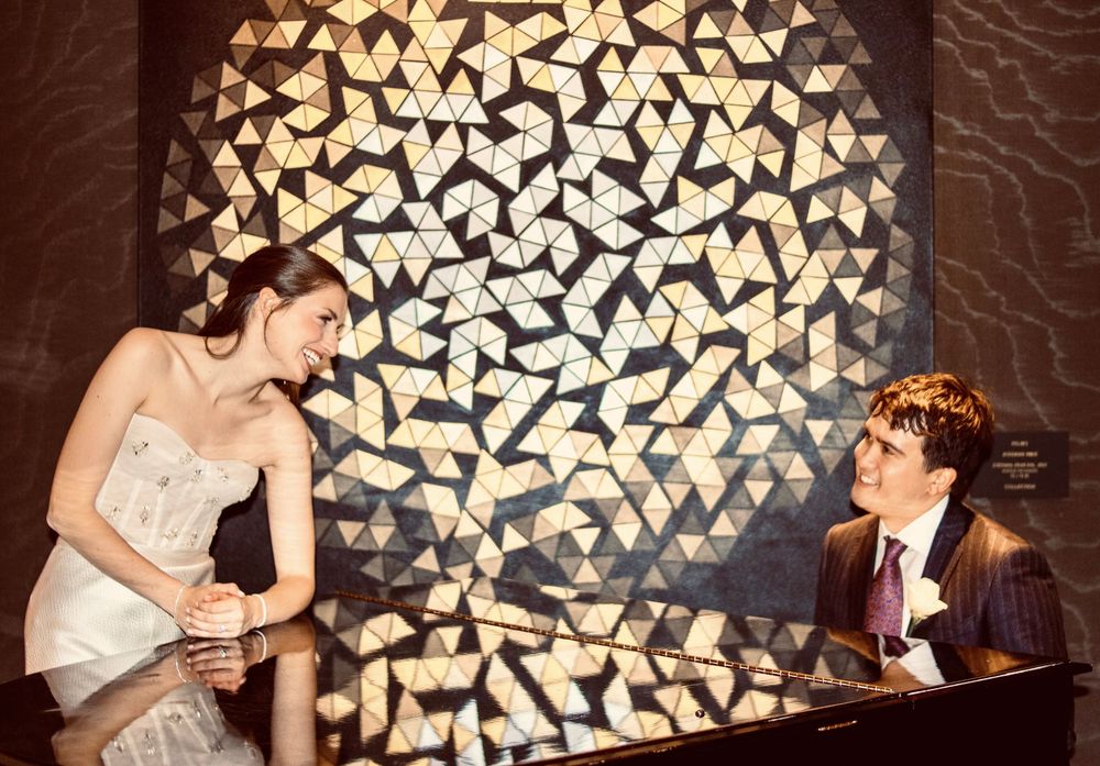 Bride and groom sharing a joyful moment at a piano in front of a stunning geometric mosaic wall.