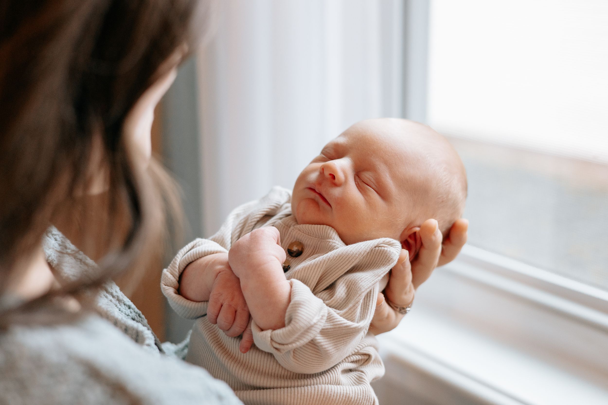 Gentle parenting moment captured by window with infant in neutral tones.
