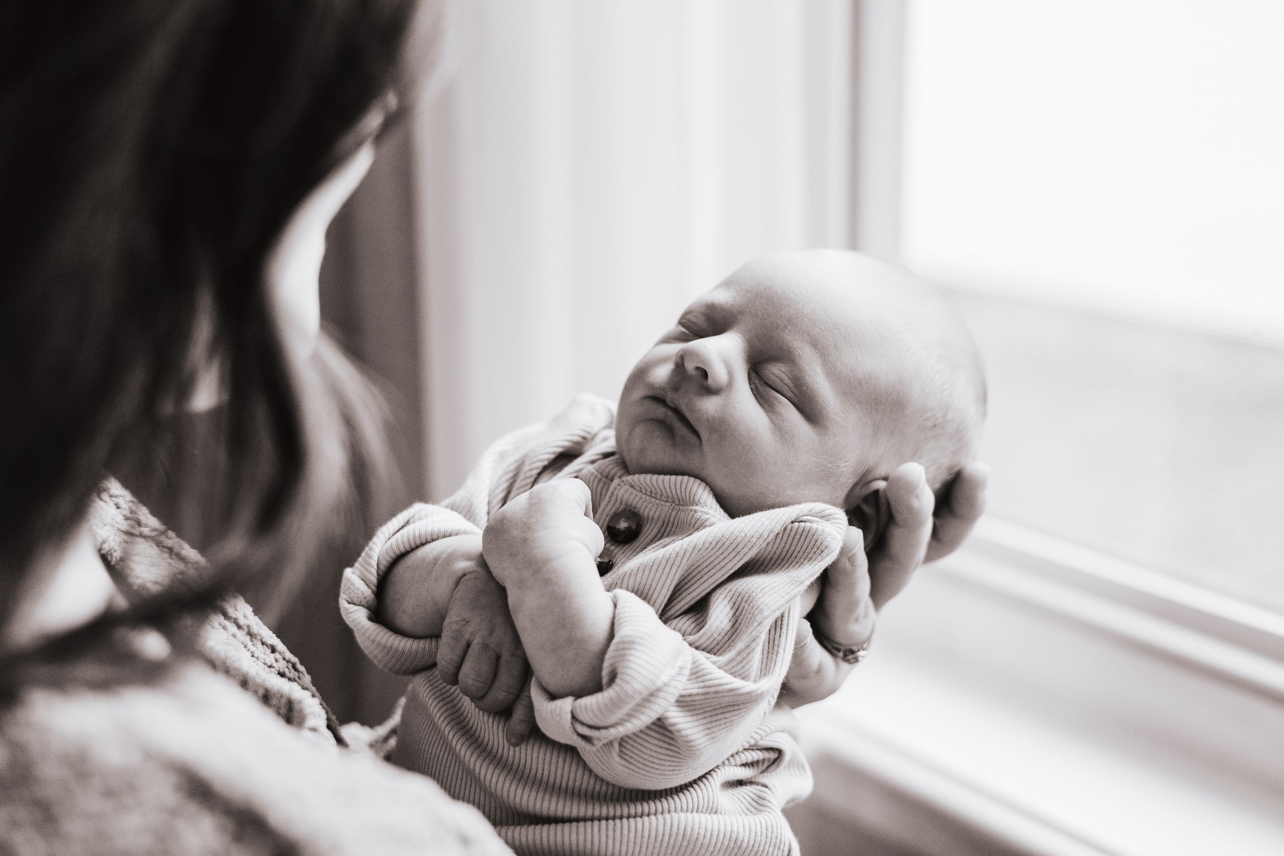 Black and white portrait of quiet moment between parent and baby near window.