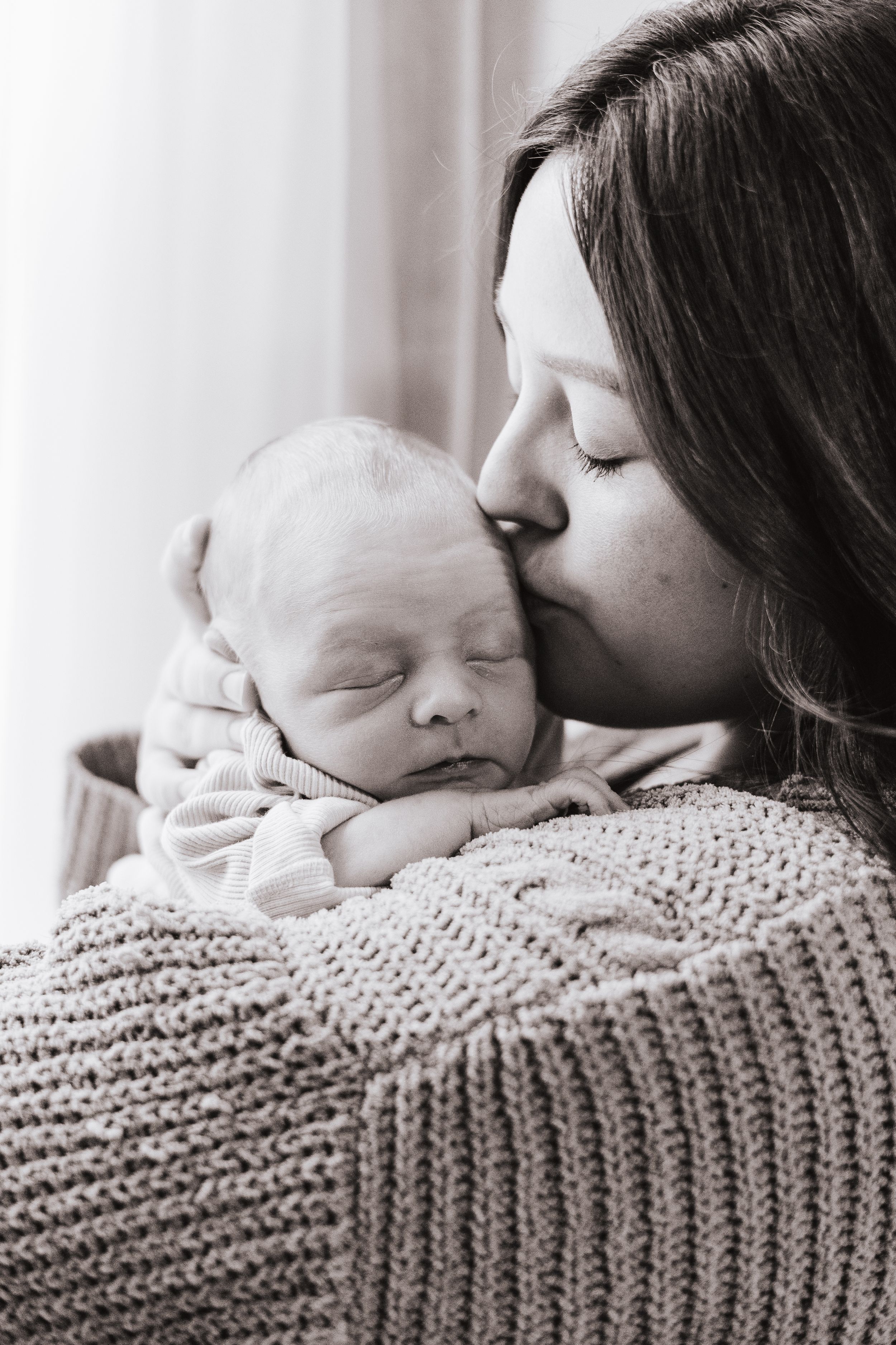 Intimate black and white photo series showing gentle kisses between parent and sleeping infant.