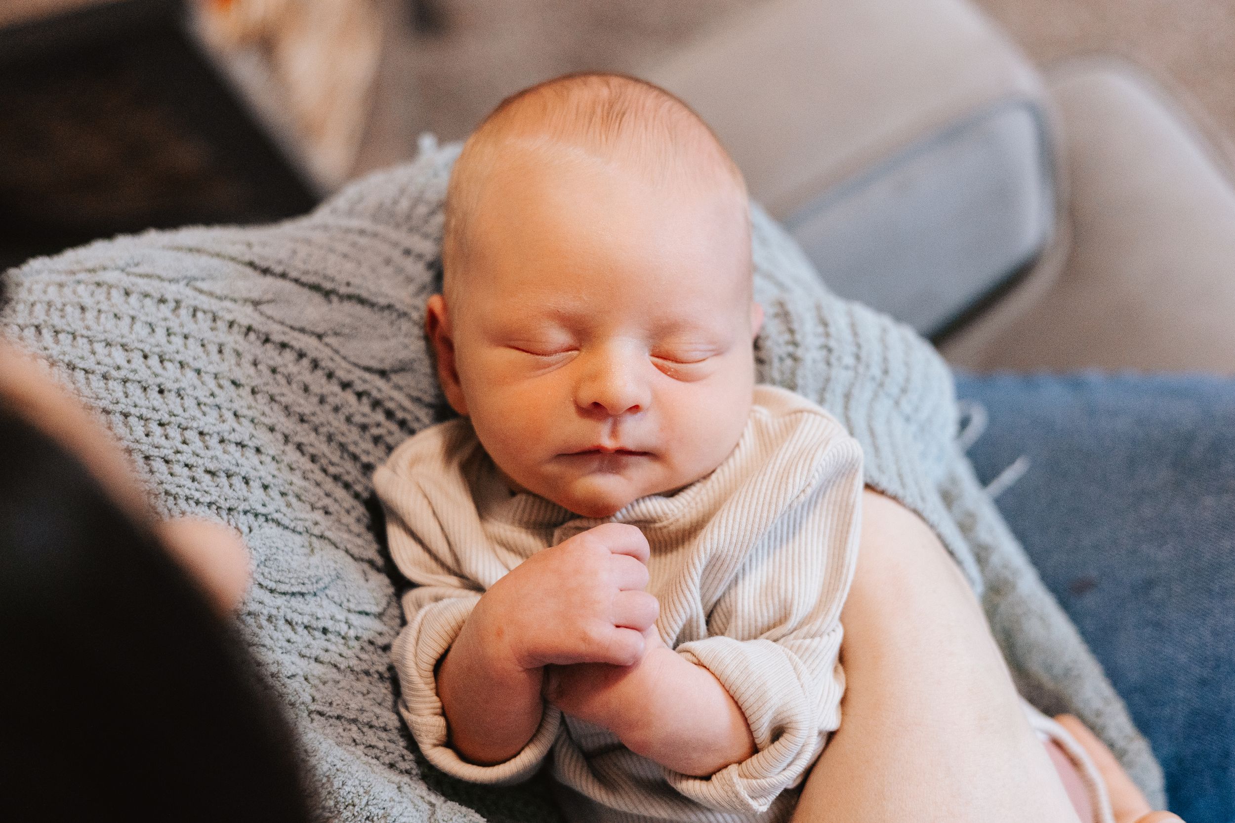Peaceful sleeping newborn baby wearing light colored onesie resting on soft knit blanket.