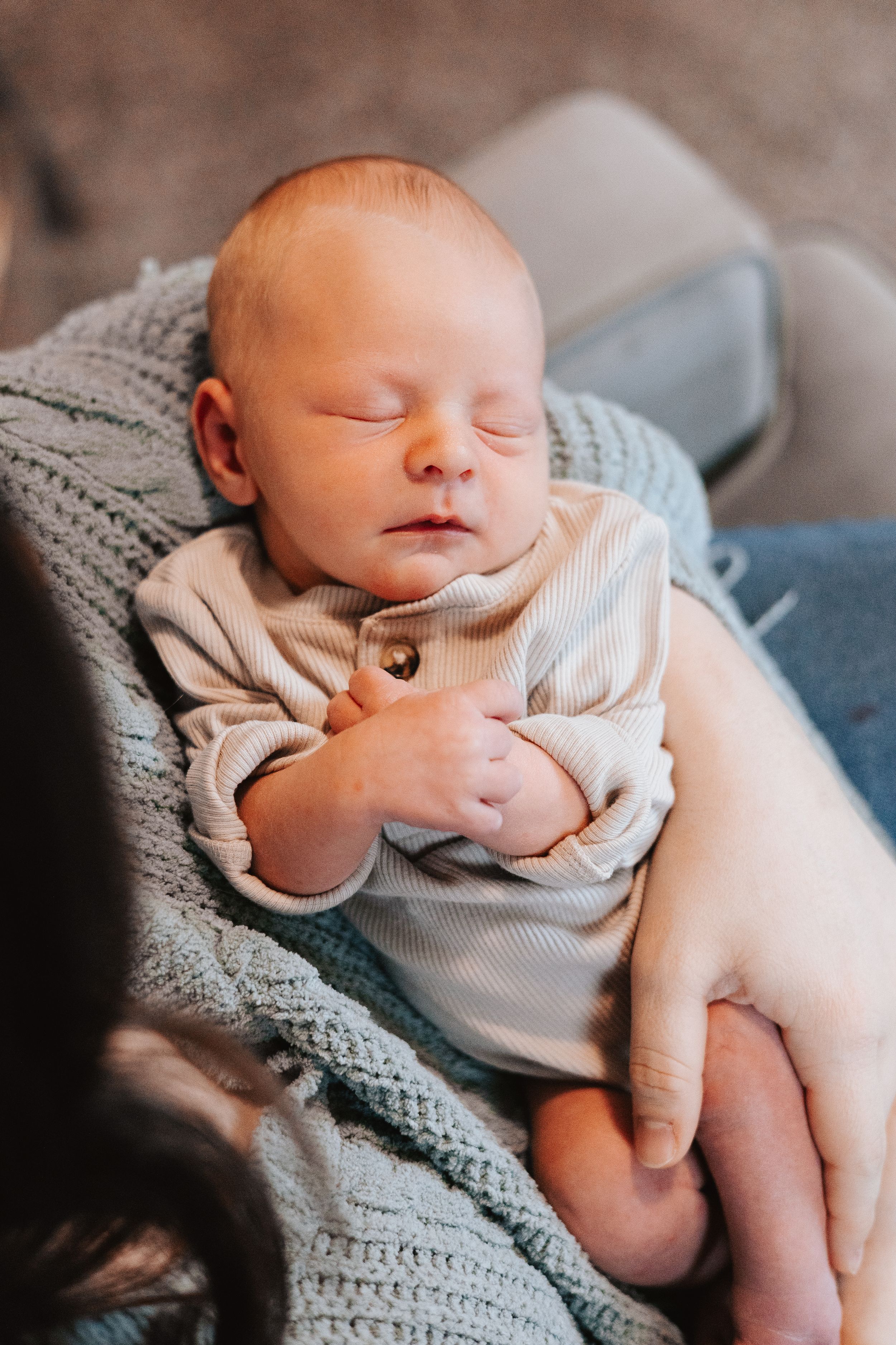 Close-up portraits of sleeping newborn baby in light colored clothing on textured gray blanket.