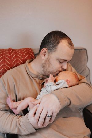 Loving sequence showing parent cradling and kissing sleeping newborn in warm lighting.