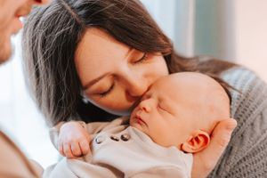 Parents sharing loving moments with their newborn baby in soft natural window light.