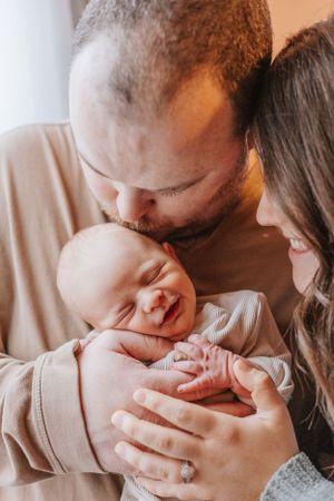 Parents in neutral tones sharing tender moments with their sleeping newborn baby.