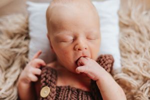 Newborn baby sleeping peacefully on furry blanket wearing knit sweater with thumb in mouth.