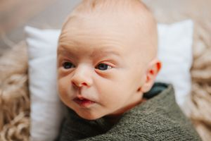 Baby wrapped in olive green swaddle lying on soft furry blanket.
