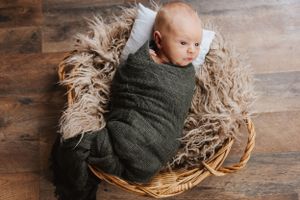 Swaddled infant resting in woven basket with fluffy blanket on wooden floor.