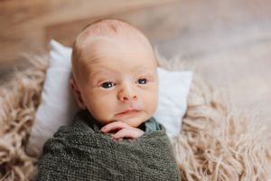 Baby wrapped in green swaddle blanket lying on textured beige surface.