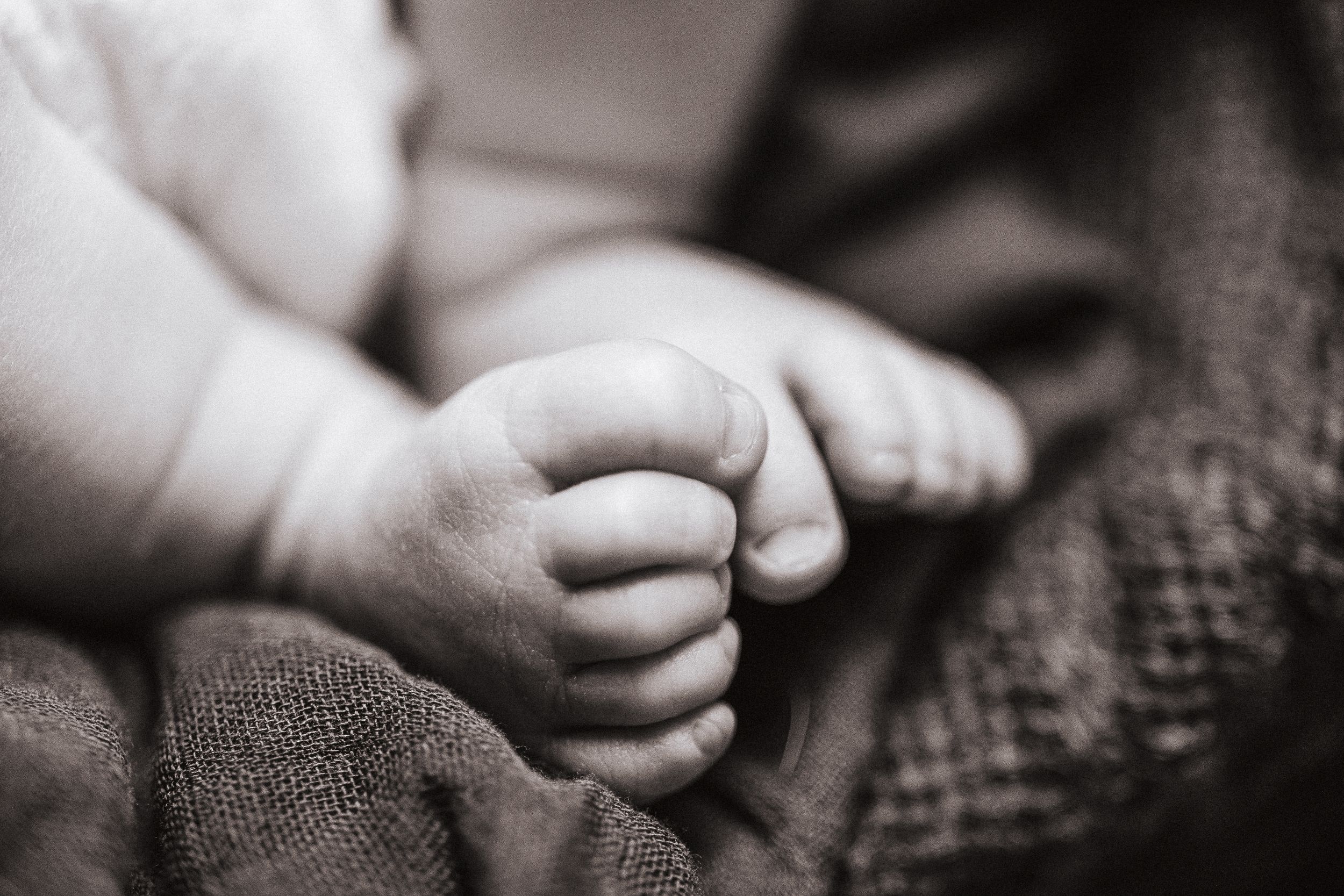 Black and white close-up of baby feet against textured fabric.