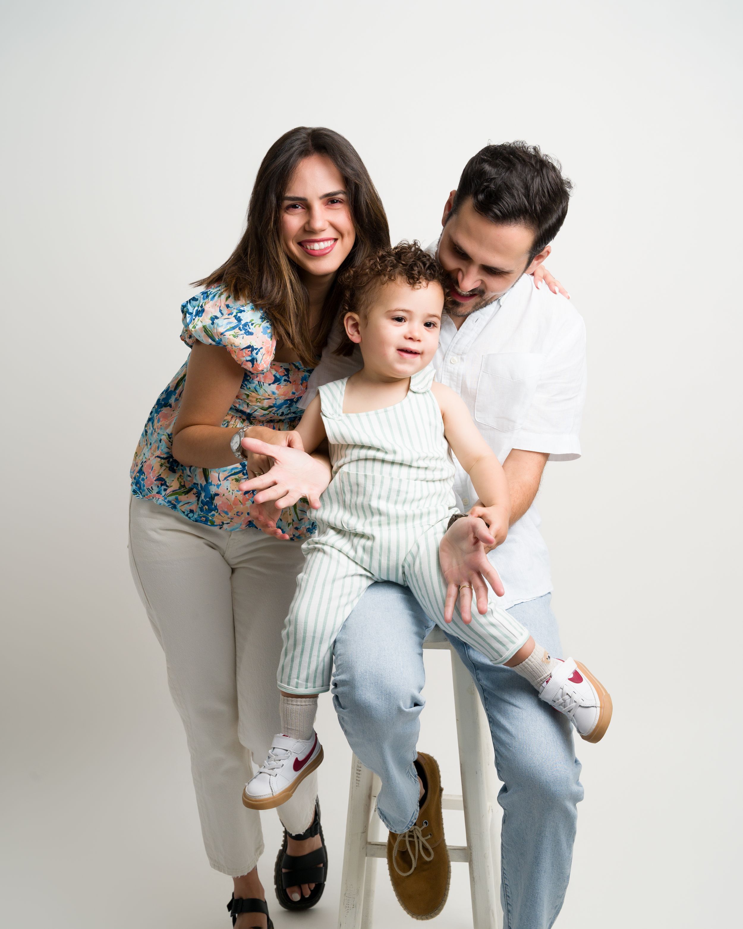Smiling family with toddler boy posing on stool in studio.
