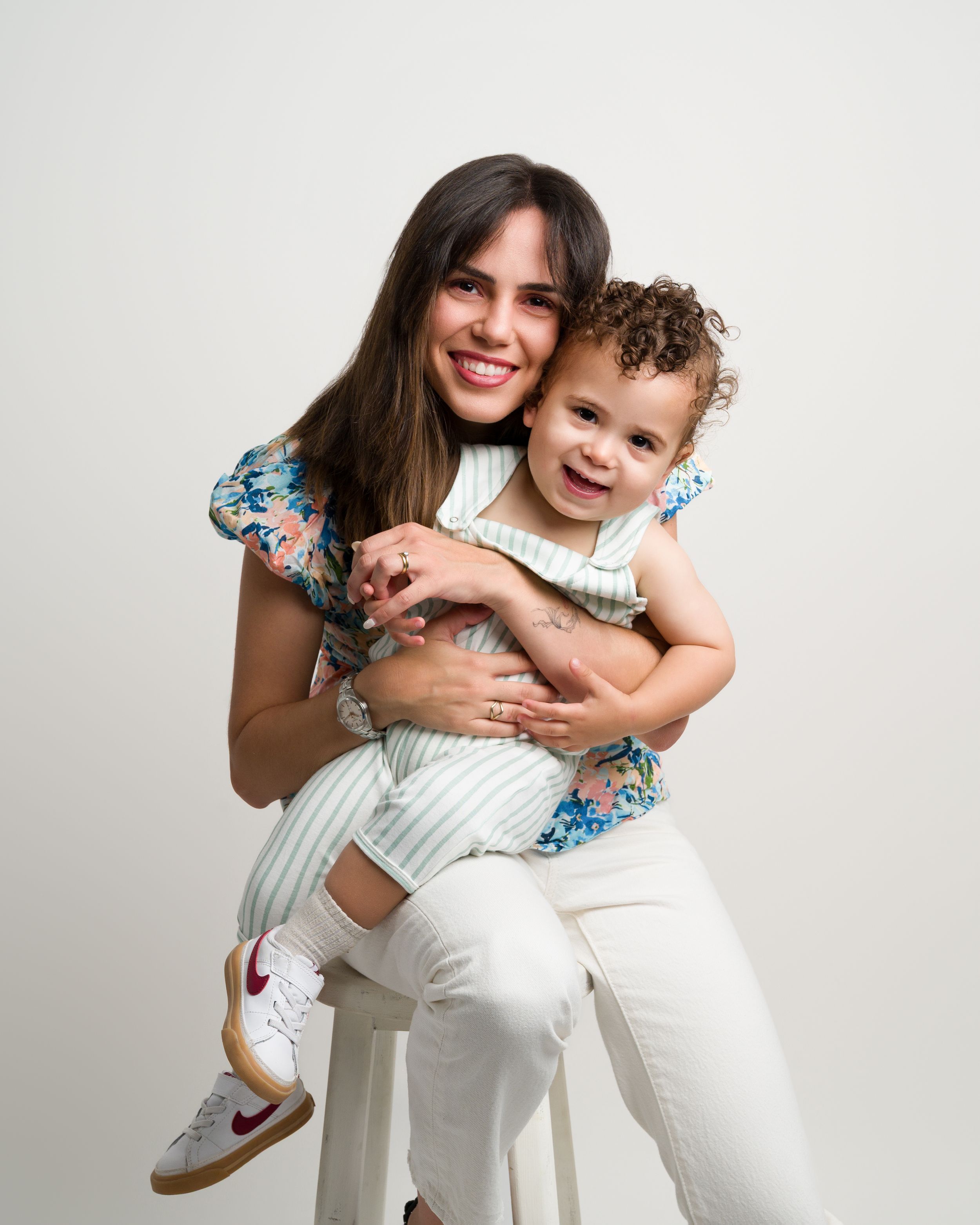 Mother sitting on stool hugging laughing toddler in studio.