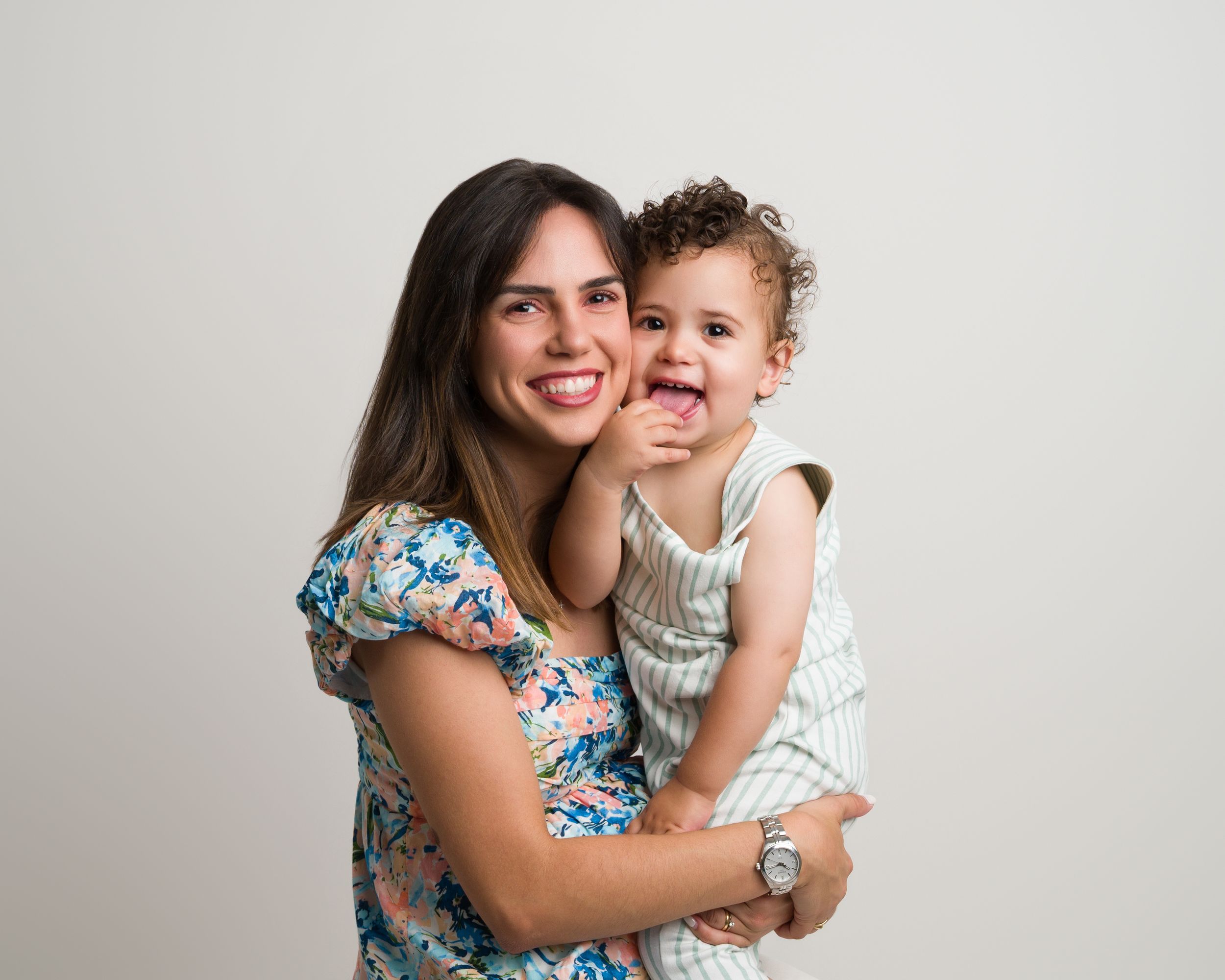 Smiling mother holding curly-haired toddler in studio portrait.
