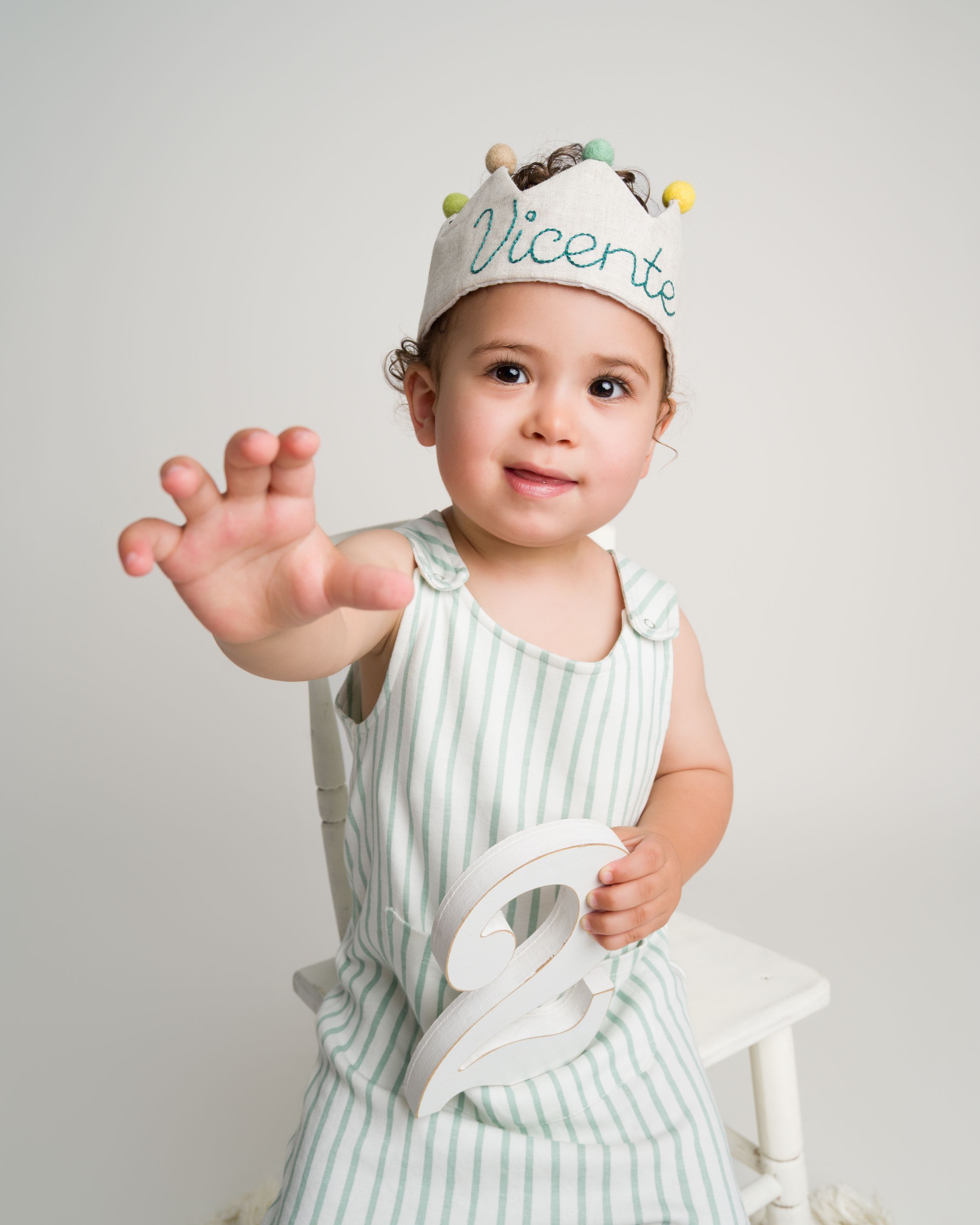 Toddler boy named Vicente wearing birthday crown holding number 2.