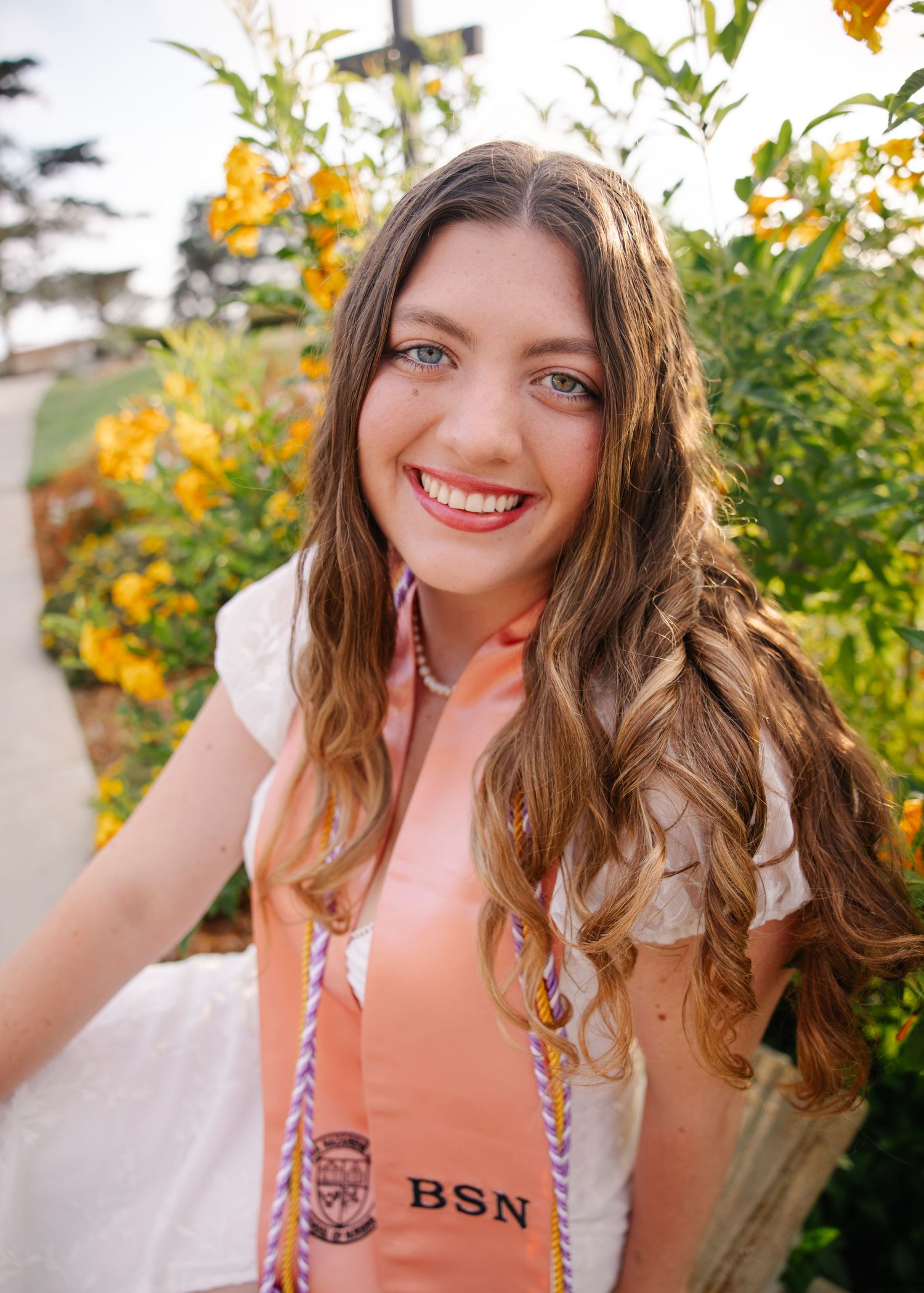 Graduate wearing pink BSN stole poses near white columns during graduation photoshoot.