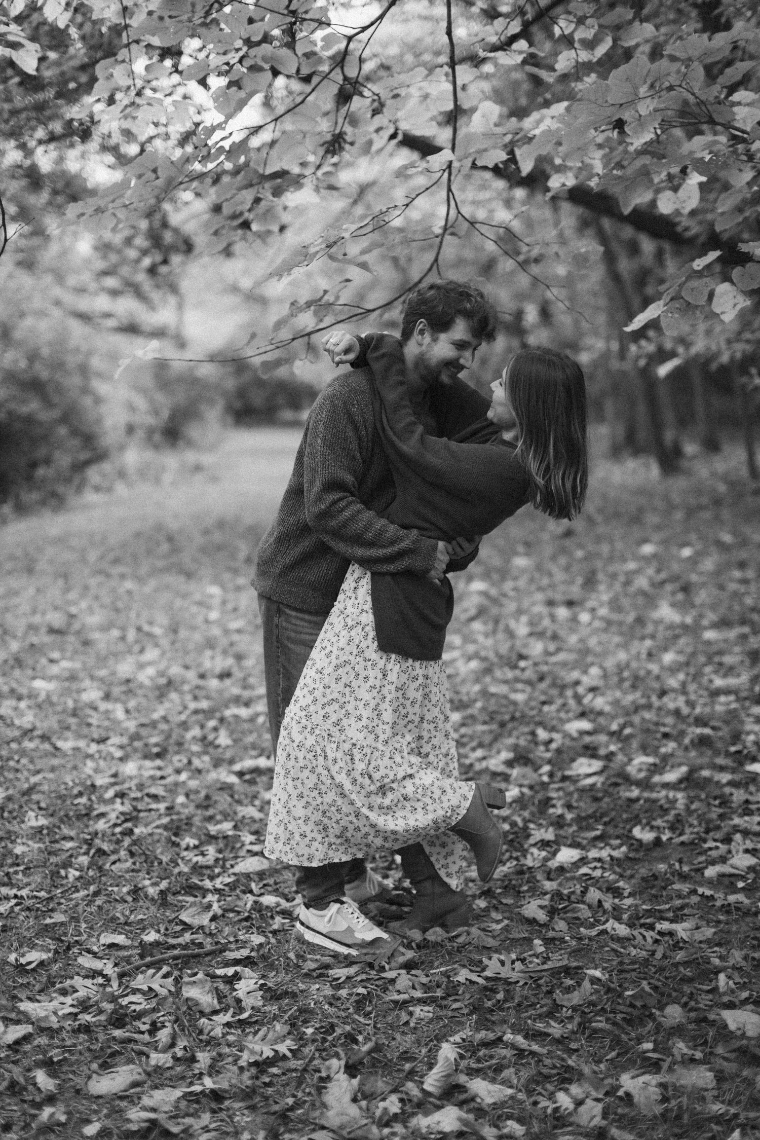 A man dips a woman under a canopy of fall trees in a black-and-white image from an engagement photo session in Kansas City.