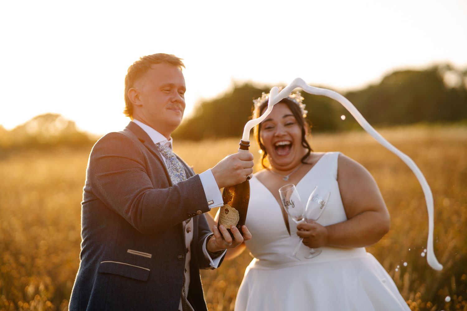 Couple popping champagne during their wedding photography and film investment celebration. medium shot both very happy at sunset.