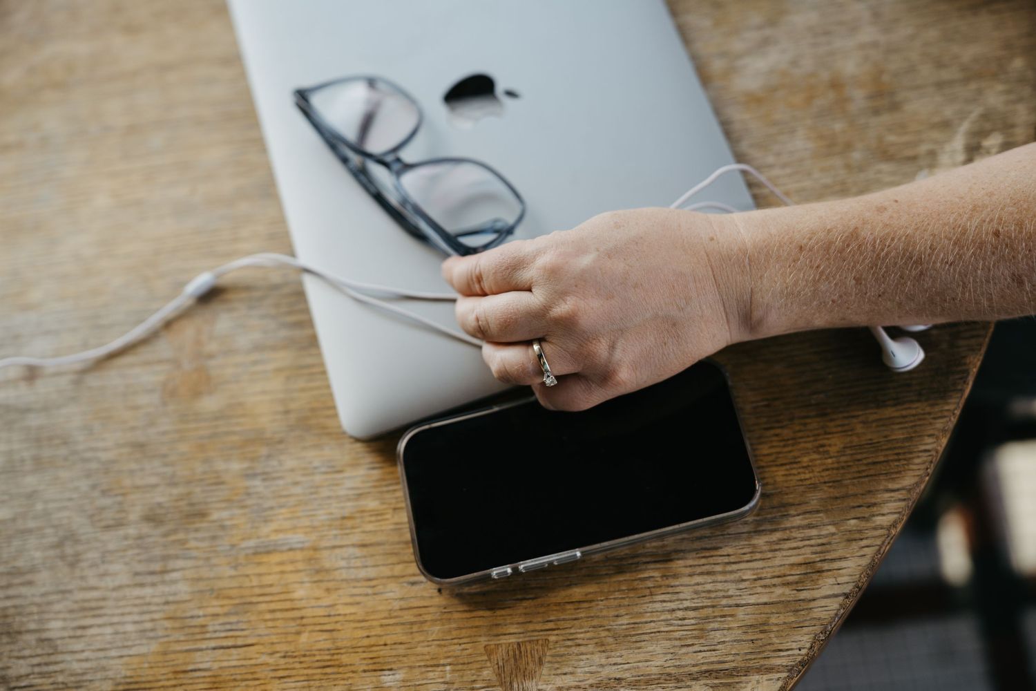 A hand holds a digital tablet or device over a rustic wooden table surface.