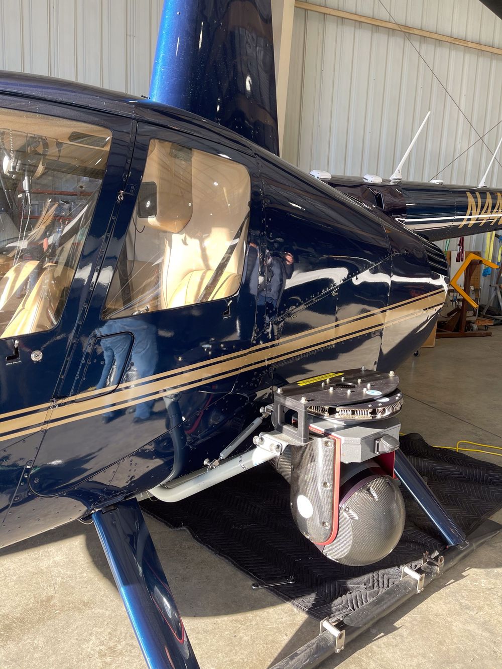Blue helicopter in hangar with mounted aerial camera gimbal system attached to the exterior skid.