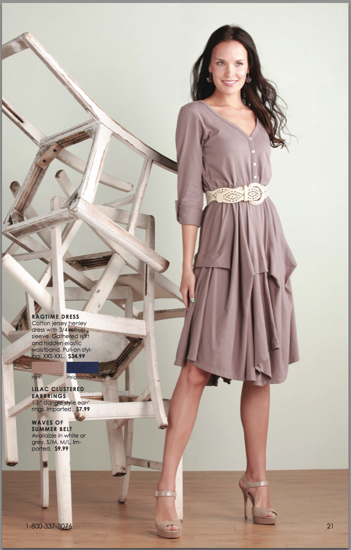 A model in a flowing taupe dress with tiered skirt and belt poses next to white wooden stairs against a neutral background.