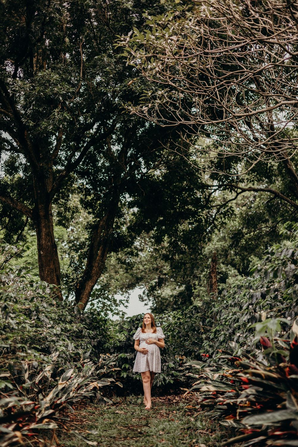 A scenic maternity photo session captured in a shaded wooded area with natural lighting.