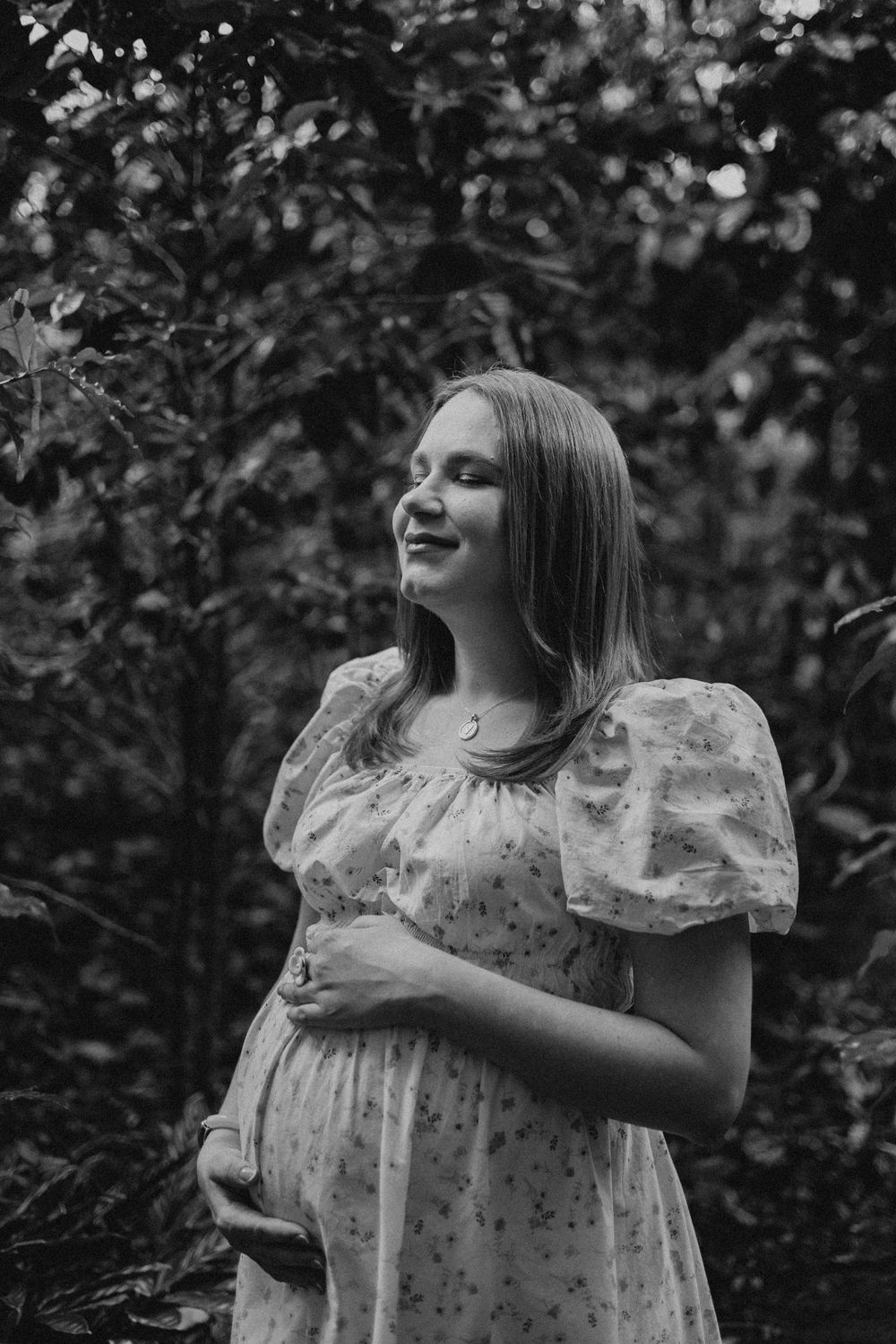 A woman in a floral dress poses playfully in a black and white outdoor portrait.