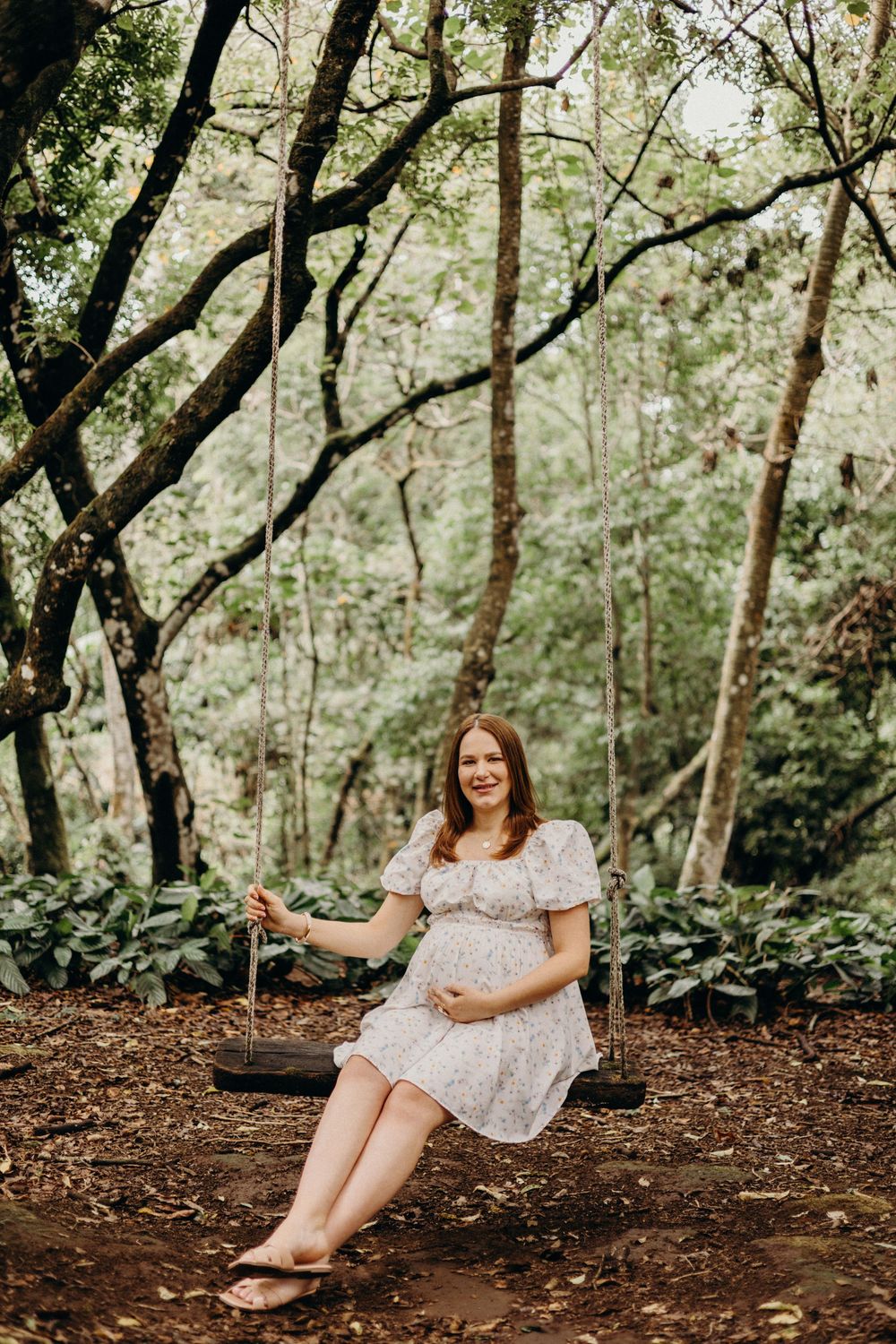 A maternity photoshoot in a wooded setting with someone wearing a white lace dress.
