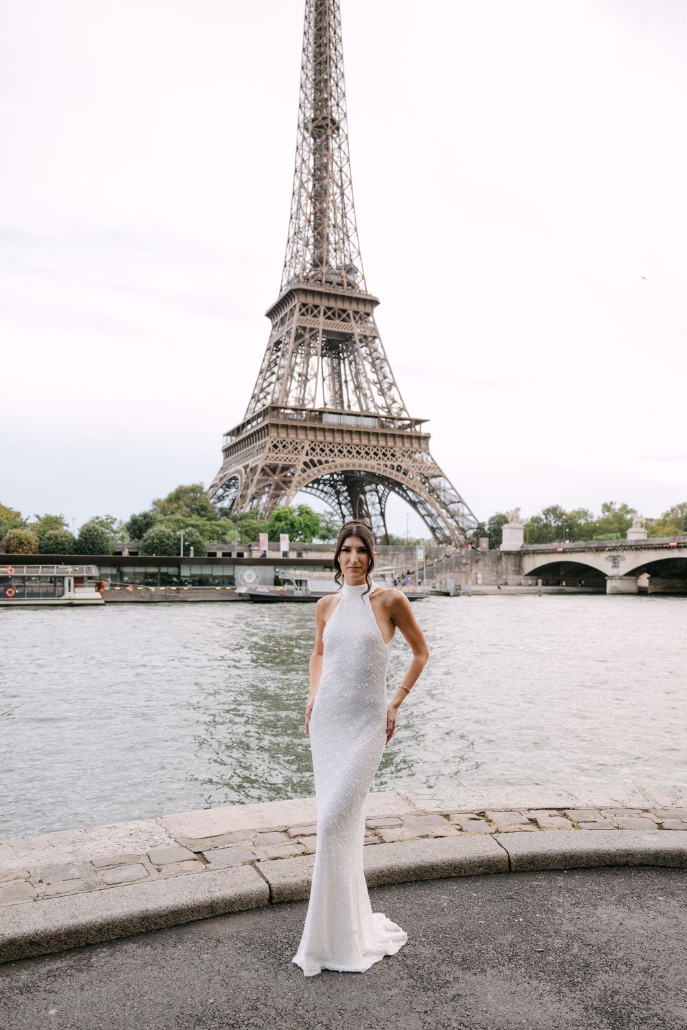 A bride poses along the Seine River with the iconic Eiffel Tower in the background.