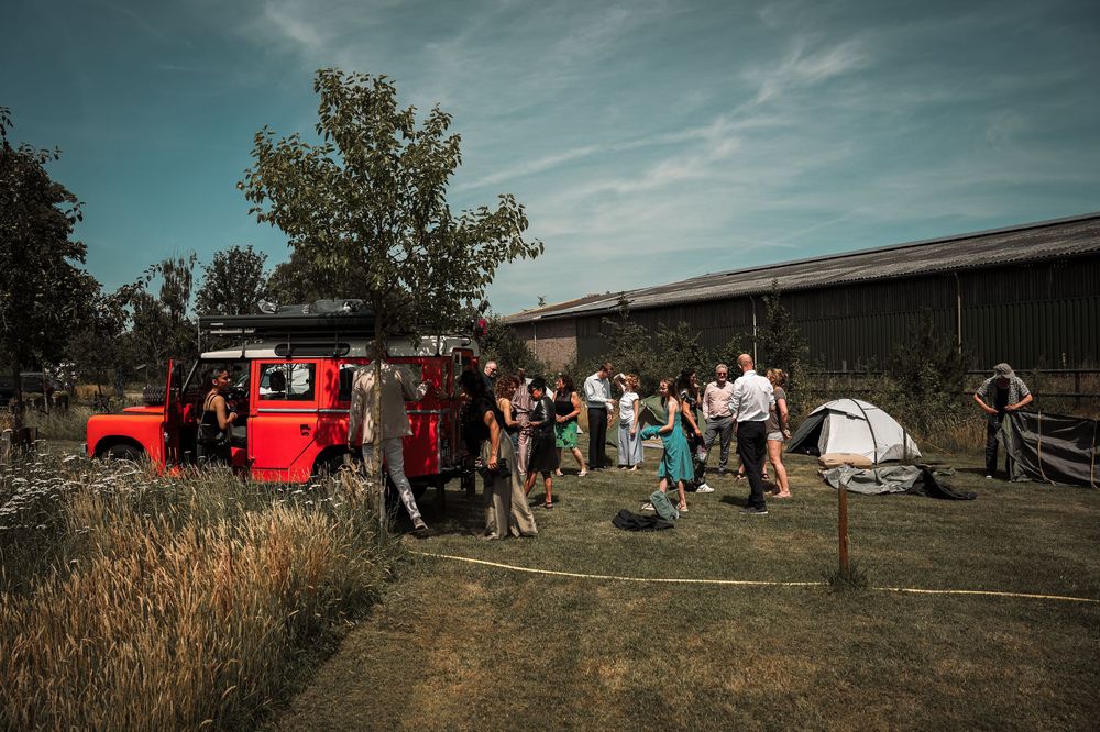 Panoramic view of outdoor festival setup with red tents and scattered groups of people gathering on grassy field.