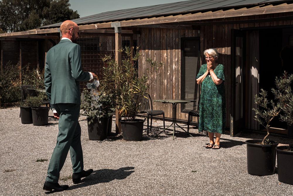 Couple in green attire walking together at a rustic outdoor venue with wooden buildings and gravel paths.