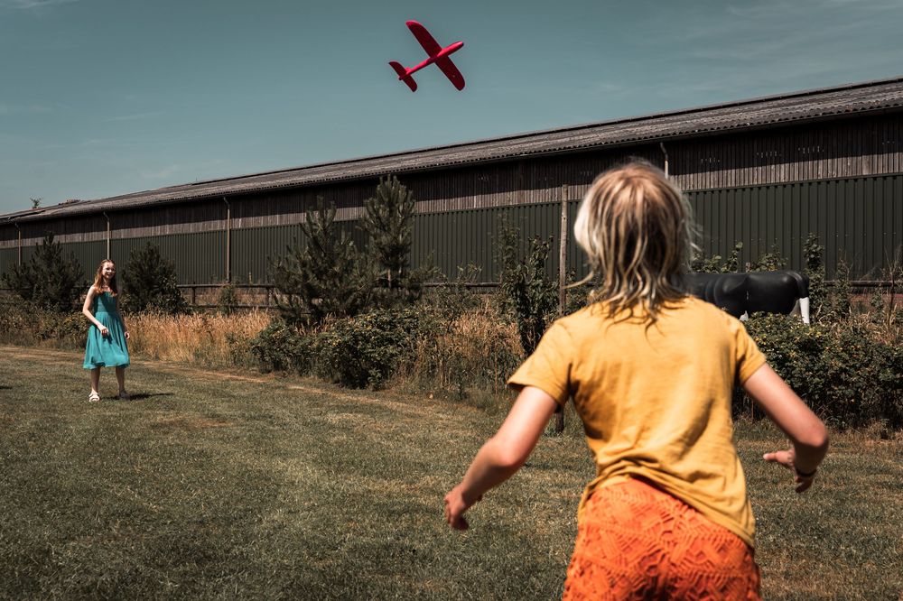 A small red airplane flies across a moody blue sky with dark clouds in the background.