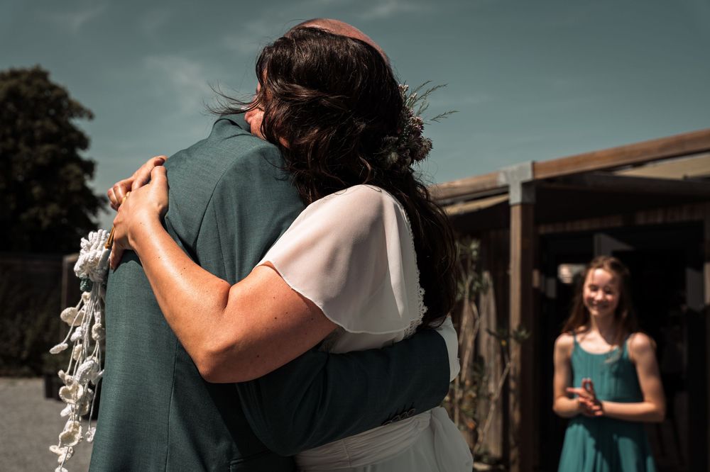 Romantic outdoor photoshoot with couple embracing against a moody blue sky backdrop.