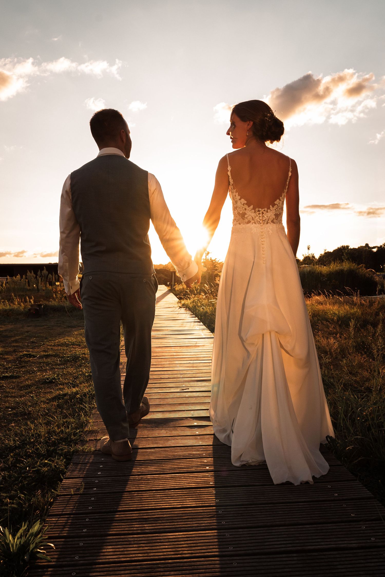 Couple walking on wooden boardwalk at sunset with warm golden light creating romantic silhouettes.