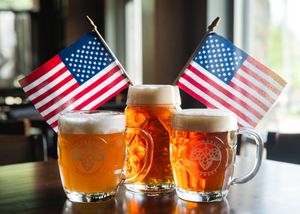 Three glasses of golden beer with American flags displayed in a patriotic bar setting.