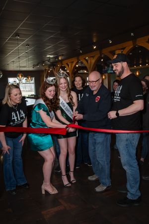 A group of people gather around a red velvet rope at what appears to be an indoor venue or event space.