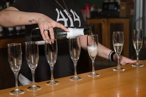 Champagne being poured into a row of elegant flute glasses lined up on a wooden bar counter.